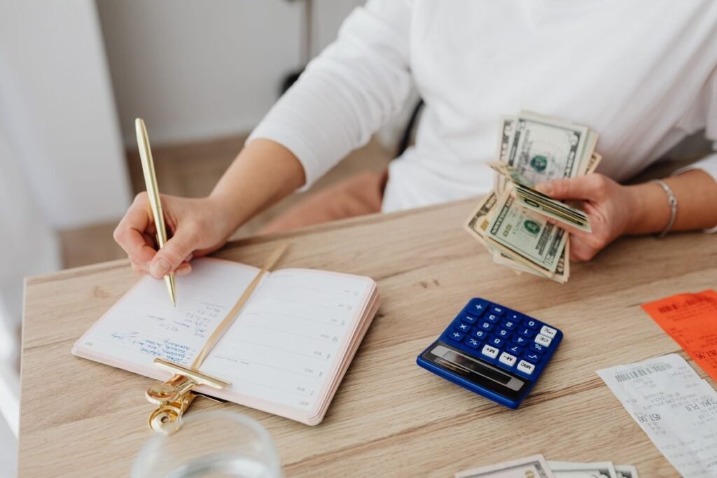 Adult holding cash and writing in planner while using a calculator at home