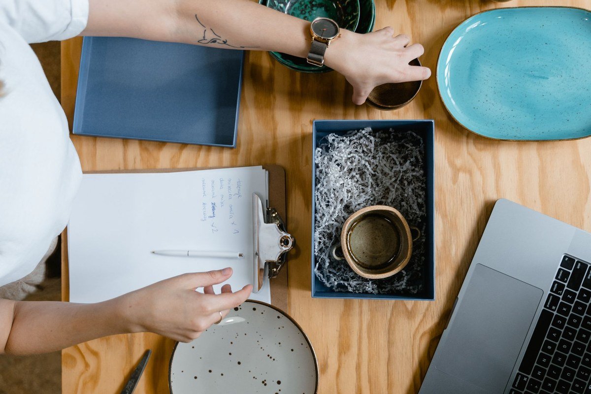 Things you can sell on Instagram: a seller packing a handmade ceramic mug into a box for shipping, with a laptop and clipboard on the table.